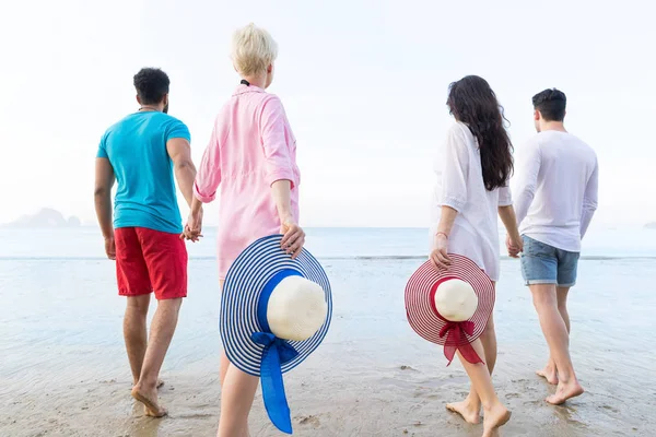 若者グループがビーチで夏の休暇に、戻って海辺を歩いている友人の背面図 — ストック写真