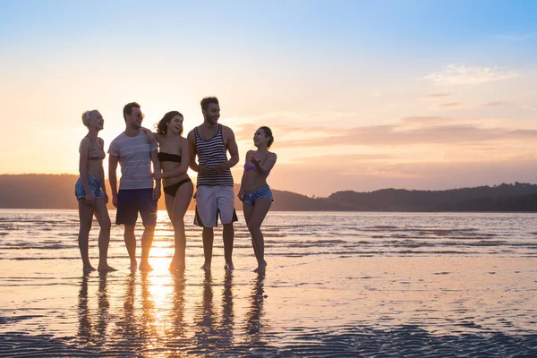 Młodzi ludzie grupy na plaży w wakacje zachód, szczęśliwy uśmiechający się przyjaciół spaceru nadmorskim — Zdjęcie stockowe