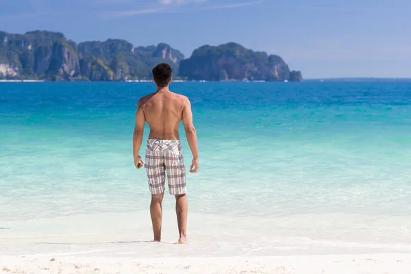 Νεαρός άνδρας στην παραλία καλοκαιρινές διακοπές, άντρας στέκεται πίσω παραθαλάσσια μπλε νερό — Φωτογραφία Αρχείου