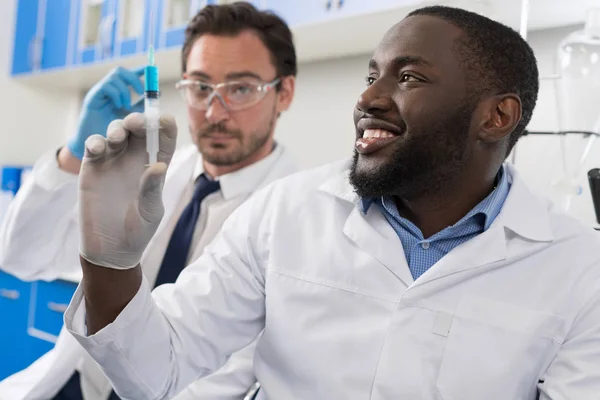 两个男的实验室科学家考察样品注射在注射器，混合种族医生在实验室研究结果的化学研究 — 图库照片