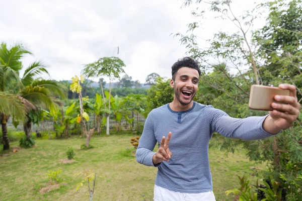 Hombre latino sonriente feliz tomando foto selfie sobre el paisaje verde de la selva tropical en el teléfono inteligente celular —  Fotos de Stock