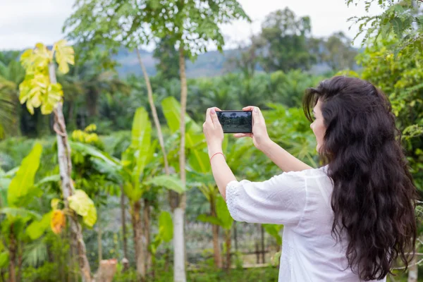 Mujer tomando foto del paisaje del bosque tropical en el teléfono inteligente celular Volver Vista trasera — Foto de Stock