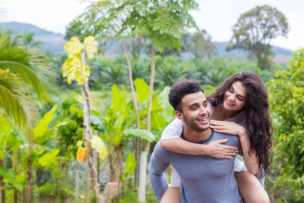 Glücklicher lateinischer Mann trägt Frau auf dem Rücken, junges Paar über grüne tropische Regenwaldlandschaft — Stockfoto