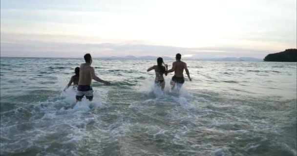 Två par körs i havet vatten gör Splash hålla händer, grupp vänner på stranden vid solnedgången att ha kul — Stockvideo