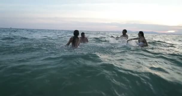 Gruppe fröhlicher Freunde schwimmt im Meer bei Sonnenuntergang junge Leute planschen im Wasser und amüsieren sich am Strand — Stockvideo