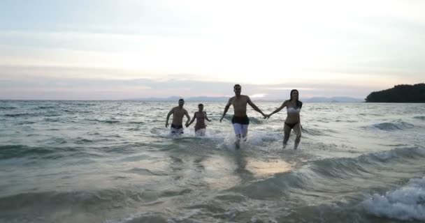 Zwei Paare laufen aus dem Wasser Meer Händchen haltend, junge Freunde Gruppe am Strand bei Sonnenuntergang Spaß haben Mix Rennen Männer und Frauen — Stockvideo