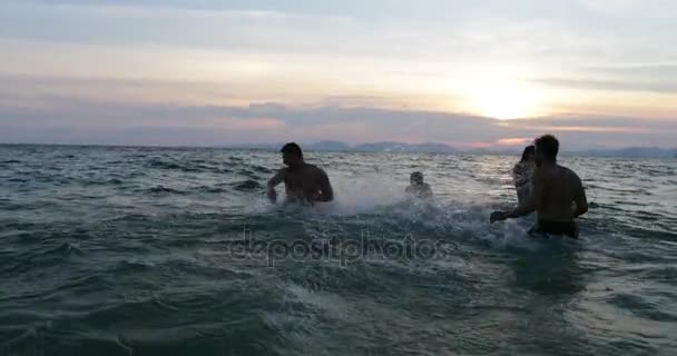 Grupo de amigos salpicando no mar ao pôr do sol, pessoas alegres jovens nadando na praia juntos durante as férias de verão — Vídeo de Stock