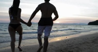 Çift denizde geri elele mutlu erkek ve kadın arkadan görünüş kumsalda gün batımında çalıştırın