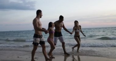 Arkadaş grubu yürüyerek Beach batımında, akşamları deniz konuşurken el ele tutuşarak iki turist Çift