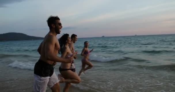 Grupp människor på stranden vid solnedgången körs i havet stänk Mix Race glada vänner på semester — Stockvideo