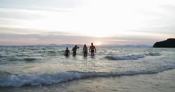 Grupp av människor som kör från havet i solnedgången, glada unga vänner tillsammans på stranden under sommarlovet — Stockvideo