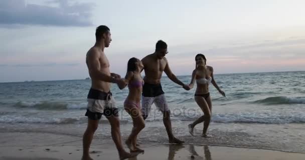 Grupo de amigos caminan playa al atardecer, dos turistas pareja sosteniendo las manos hablando por la noche en la playa — Vídeo de stock
