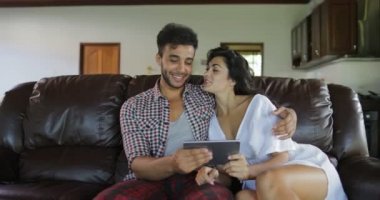 Oturma odası, genç adam ve kadın Online Modern Daire iç tarama konuşurken Tablet bilgisayar kullanarak Koç oturan çift kucaklama