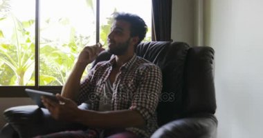 Tablet bilgisayar koltukta, evde, işadamı Mix yarış adam fotoğrafçı dijital aygıt kullanarak oturan çizim ile çalışan genç adam