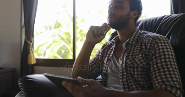 Young Man Working With Drawing Tablet Computer Sitting In Armchair At Home, Smiling Businessman Mix Race Photographer Using Digital Device — Stock Video