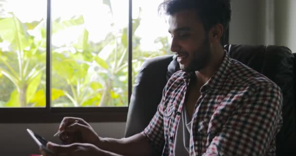 Young Man Working With Drawing Tablet Computer Sitting In Armchair At Home, Smiling Businessman Mix Race Photographer Using Digital Device — Stock Video