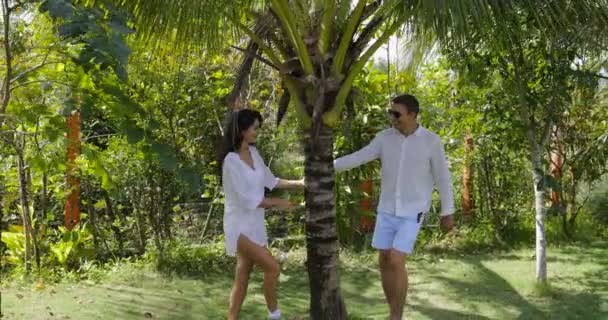 Caminhada de casal no jardim tropical Stand Under Palm Tree Talking, homem feliz e mulher ao ar livre — Vídeo de Stock