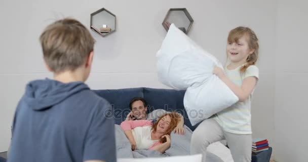 Familia feliz en el dormitorio por la mañana, dos niños luchando almohadas sobre padres sonrientes felices acostados en la cama — Vídeos de Stock