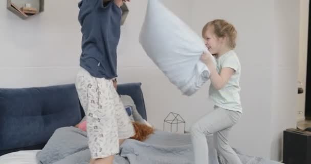 Enfants heureux s'amusant dans la chambre des parents combattant des oreillers le matin tandis que la mère et le père allongeant le lit de Pn riant — Video