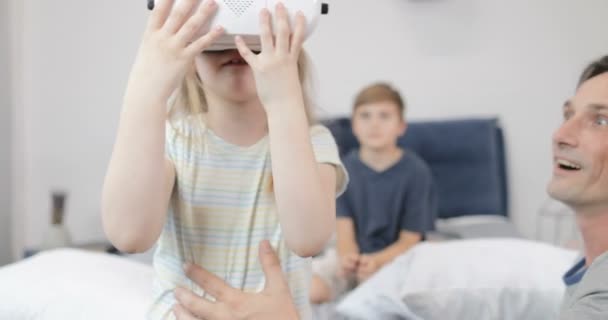 Счастливый отец держит маленькую девочку в очках виртуальной реальности в спальне, семейное утро вместе дома — стоковое видео