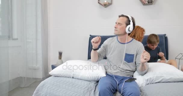 Cheerful Father Using New Headphones Listening To Music In Bedroom Over Mother Communicating With Son Spending Time Together With Children In Morning — Stock Video