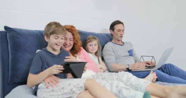 Famille passer la matinée ensemble sur le lit des parents avec des enfants en utilisant la tablette et ordinateur portable dans la chambre — Video