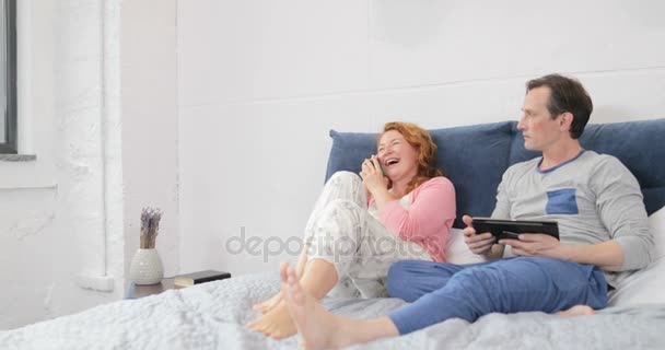 Svartsjuk Man tittar kvinnan talar i mobiltelefon ringa skrattande sitter på sängen i par sovrum — Stockvideo