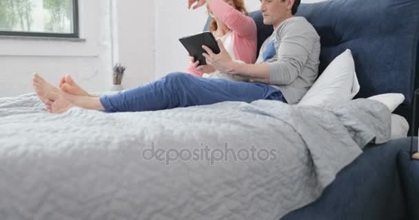 Coupe Sitting On Bed Using Digital Tablet Computer, Embracing Man And Woman Talking In Bedroom Browsing Internet — Stock Video