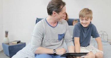 Baba ve oğul aile yatak odasında birlikte vakit konuşmak yatağın üstüne oturan dijital Tablet tutun