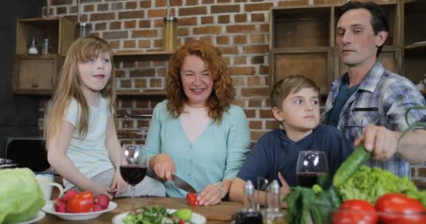 Οικογένεια μητέρα βοηθώντας με μαζί μαγειρική στην κουζίνα γονείς με δύο παιδιά, προετοιμασία φαγητού στο σπίτι μιλάμε κόψιμο λαχανικών για σαλάτα — Αρχείο Βίντεο