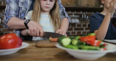 Baba yardım kız akıllı telefon mutfak anne iki oğlu ve annesi kullanım hücre ise sebze kesmek için hazırlanıyor gıda, mutlu bir aile birlikte çocuklar