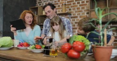 Baba ve kızı birlikte oğlu evde iletişim anne kullanarak Tablet dijital bilgisayar mutlu aile süre ile konuşurken mutfak pişirme sebze doğrama