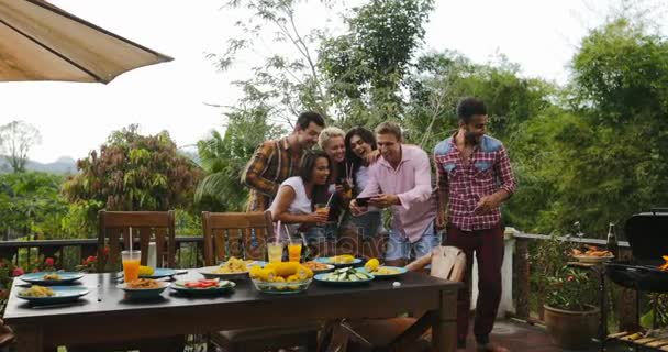 Les jeunes parlent à l'aide de téléphones intelligents cellulaires tandis que l'homme latin cuisine barbecue amis groupe joyeuse danse rassemblement sur terrasse d'été — Video