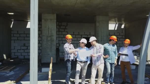 空中射击的讨论的项目计划与建筑师和承包商使用蓝图的建筑工地上的建设者团队 — 图库视频影像