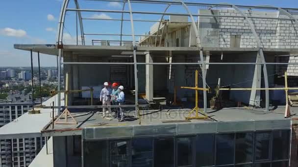 Vista aérea do local de construção com a equipe de construtores no telhado discutindo o plano do projeto — Vídeo de Stock