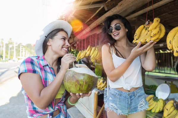 Gyönyörű lányok kiválasztása utcai piac és ital kókusz boldog vonzó a turisták a banán, az ázsiai gyümölcs bazár — Stock Fotó