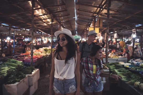 Turistas caminando entre filas en el exótico mercado tropical Jóvenes eligiendo frutas y verduras frescas en el bazar asiático —  Fotos de Stock