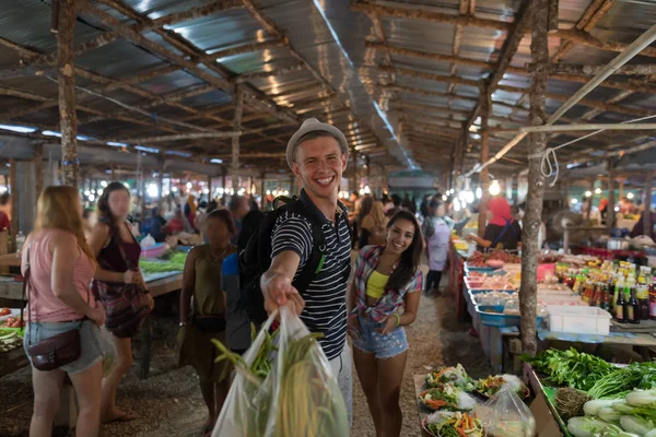 Feliz pareja sonriente sostiene bolsas con verduras en el mercado callejero alegre hombre y mujer de compras juntos en el bazar exótico —  Fotos de Stock