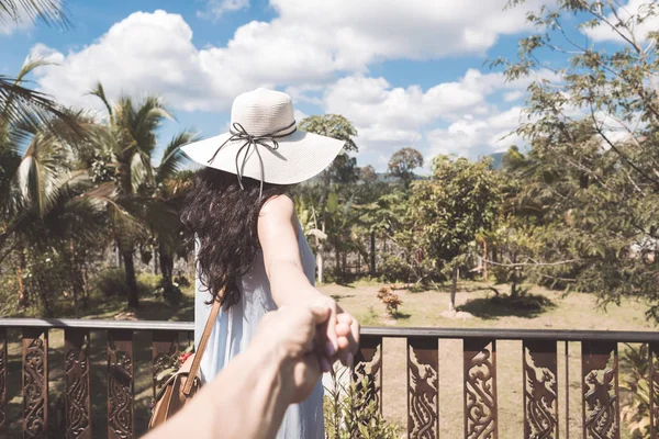 Rückansicht der jungen Frau mit Hut und Kleid auf Balkon oder Terrasse genießen tropische Waldlandschaft hält männliche Hand — Stockfoto