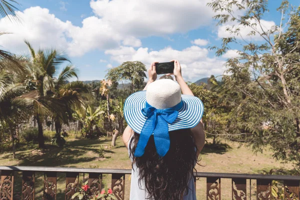 Mulher nova no chapéu faz a fotografia da paisagem tropical da floresta da varanda ou do terraço — Fotografia de Stock