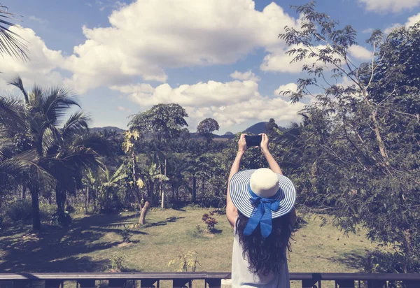 Hermosa mujer en sombrero haciendo foto del bosque tropical desde el balcón del hotel o la terraza vista trasera — Foto de Stock
