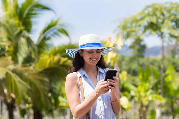 Jovem mulher mensagens com celular inteligente telefone sobre floresta tropical e céu azul bela morena menina conversando online — Fotografia de Stock