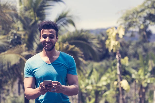 열 대 숲 배경, 온라인 채팅 하는 젊은 남자의 초상화 위에 잘생긴 라틴어 남자 셀 메시징 스마트 전화 — 스톡 사진
