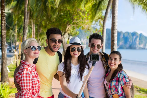 Gruppo di persone scattare selfie con action camera sul bastone mentre si cammina nel parco delle palme sulla spiaggia, felice sorridente Mix Race Friends — Foto Stock