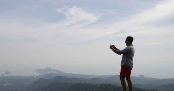 Homem no topo da montanha, turista masculino tirando foto da paisagem da manhã no celular inteligente telefone traseiro vista — Vídeo de Stock