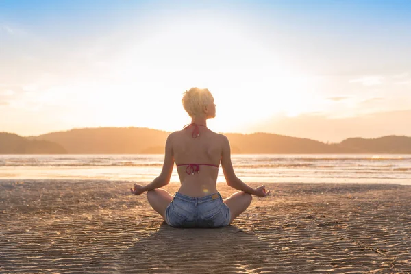 Jong meisje zittend Lotus Pose op strand bij zonsondergang, mooie vrouw beoefenen van Yoga zomervakantie meditatie Seaside — Stockfoto