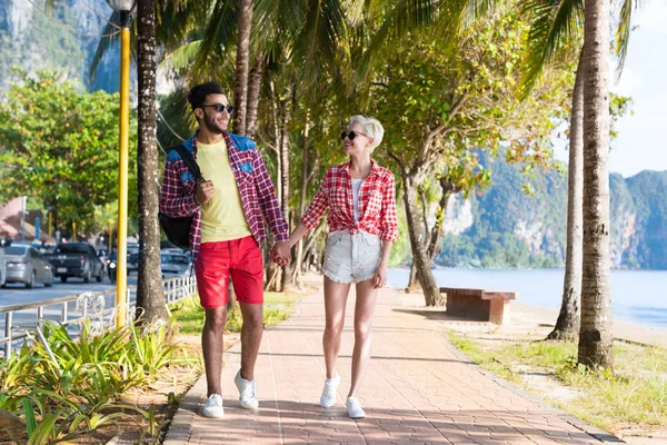 カジュアルなカップルが熱帯ヤシの木公園、夏休みに美しい若者を歩いて手をつないでください。 — ストック写真
