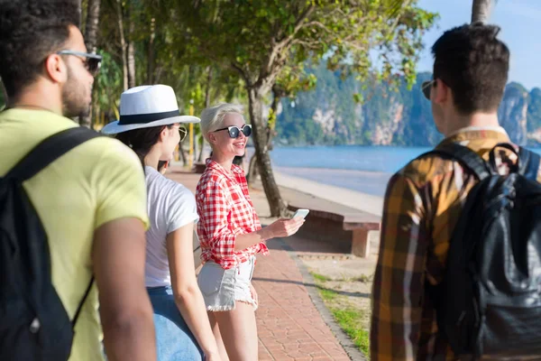 Gruppo di persone a piedi nel parco delle palme sulla spiaggia a parlare, amici turisti occasionali — Foto Stock