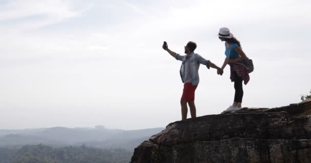 Туристы пара стоять на вершине горы решений видео пейзаж на сотовый смарт-телефоны, молодой человек и женщина путешественники держась за руки — стоковое видео