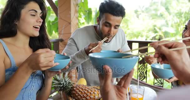 Le persone si nutrono a vicenda con deliziosi tagliatelle Cibo asiatico, Gruppo di amici si siedono a tavola sulla terrazza Vista sulla foresta tropicale — Video Stock